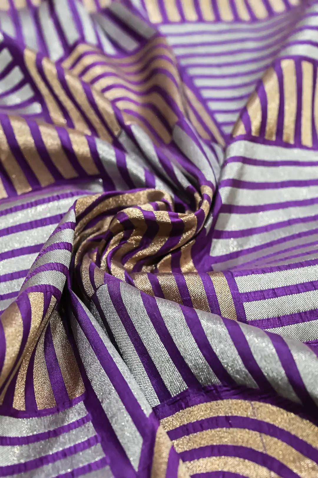 A close-up of draped fabric with a woven striped pattern in purple, metallic gold, and silver.